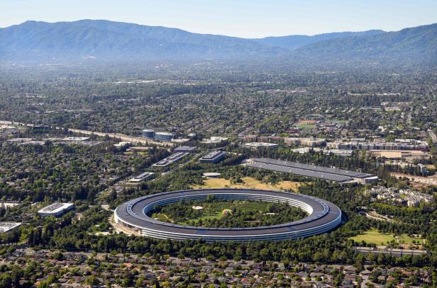 Luftaufnahme des kreisförmigen Apple Park Campus in Cupertino mit umliegenden Wohngebieten und Bergen im Hintergrund.