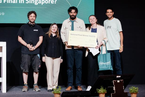 Fünf Personen stehen auf einer Bühne, eine Frau hält einen großen Scheck mit der Aufschrift „National Final Winner Austria“.
