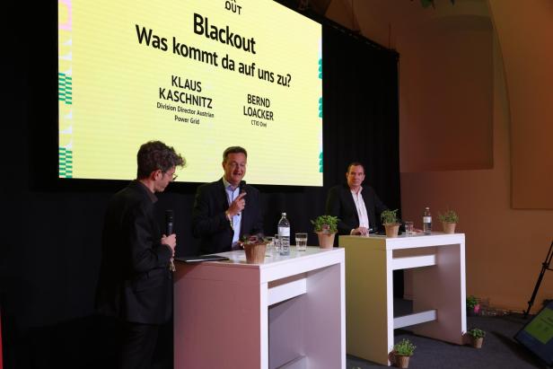 Klaus Kaschnitz und Bernd Loacker diskutieren auf einer Bühne vor einer Leinwand zum Thema „Blackout – Was kommt da auf uns zu?“.