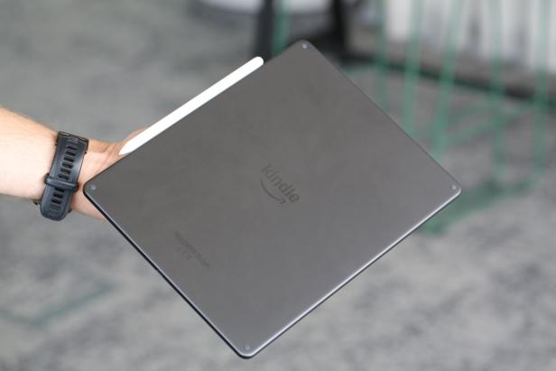 Rückseite eines Kindle Scribe Colorsoft mit Stift, gehalten von einer Hand mit schwarzer Uhr.