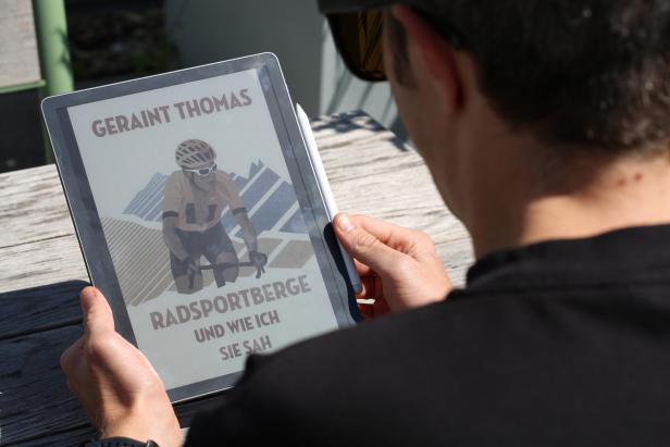 Person liest auf einem Kindle Scribe mit Farbdisplay ein E-Book über Radsportberge.