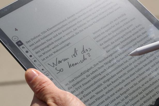 Hand hält einen E-Reader mit handschriftlicher Notiz auf dem Bildschirm und einem Stift daneben.