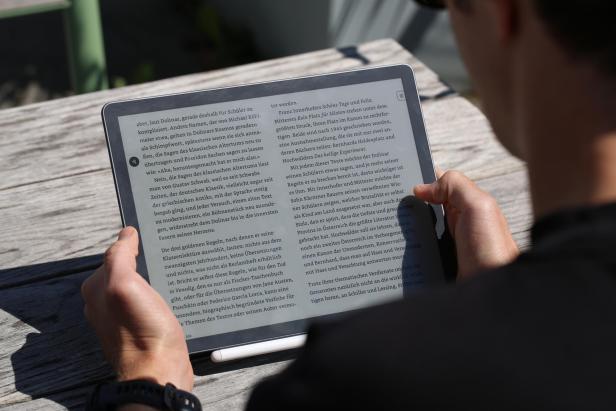 Person liest im Freien auf einem großen E-Reader mit Textanzeige im Querformat.