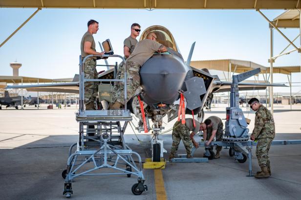 Soldaten warten einen F-35-Kampfjet unter einem überdachten Bereich auf einem Militärflugplatz.