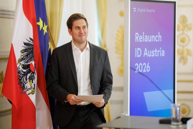 Digitalisierungsstaatssekretär Alexander Pröll hat einen Anzug an und steht im Bundeskanzleramt neben einer Österreich-Fahne