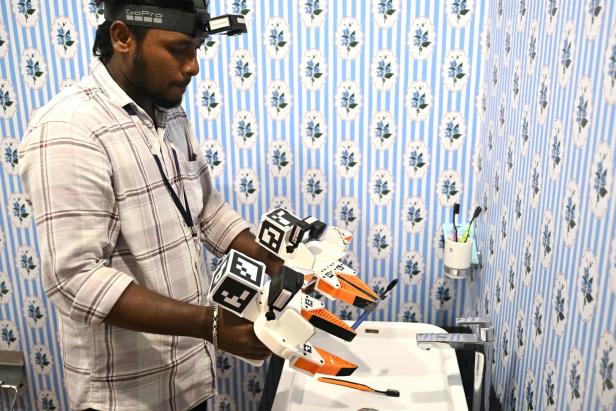 Mann mit Stirnlampe hält ein Robotergerät über einem Waschbecken im kleinen Bad.