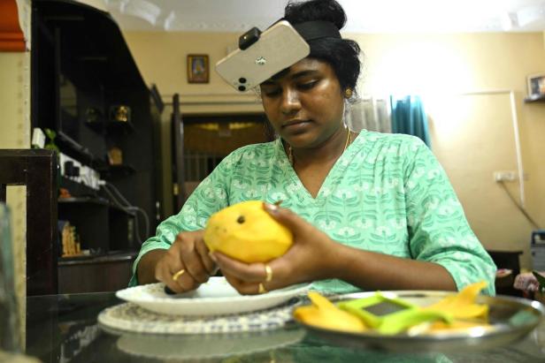 Eine Frau mit einem am Kopf befestigten Smartphone schält konzentriert eine Mango.