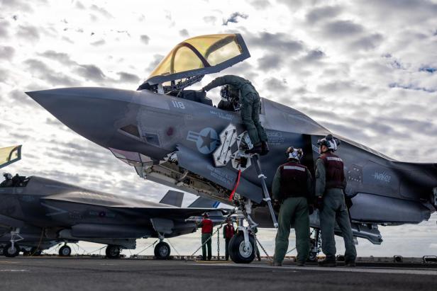 Techniker inspizieren eine geöffnete F-35 auf dem Flugdeck, während ein Pilot ins Cockpit klettert.