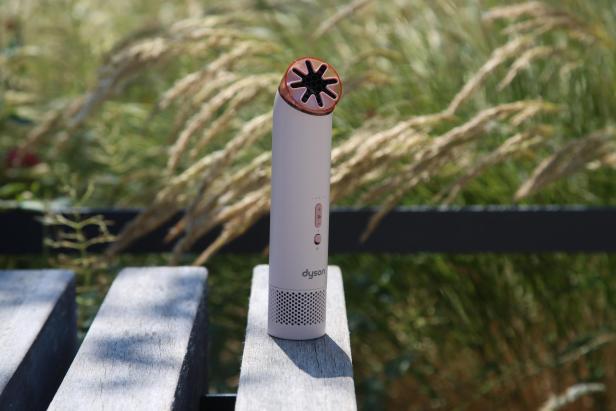 Dyson-Handventilator in Rosa auf einer Holzbank im Freien.