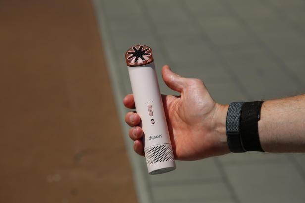 Hand hält einen rosa Dyson-Händventilator im Freien.