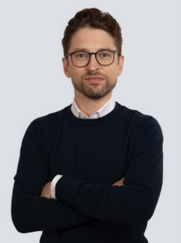 Porträt eines Mannes mit Brille und verschränkten Armen vor hellem Hintergrund.