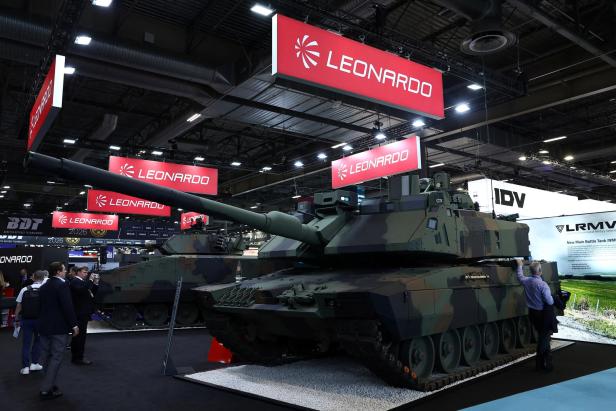 Ein Kampfpanzer von Leonardo steht auf einer Messe, während Besucher das Exponat betrachten.