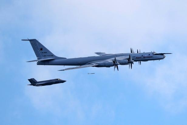 Ein russischer Tupolew Tu-142-Aufklärer fliegt vor einem F-35-Kampfjet am blauen Himmel.