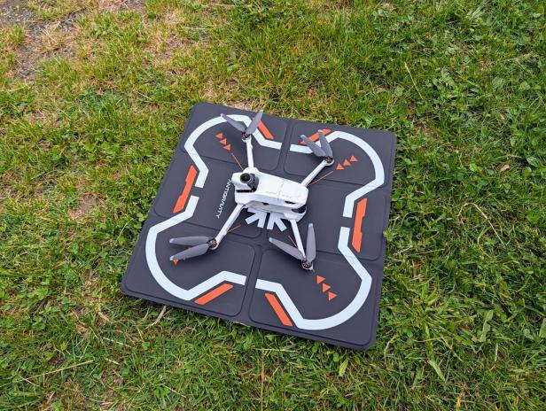 Eine Drohne liegt auf einer schwarzen Startmatte im Gras.