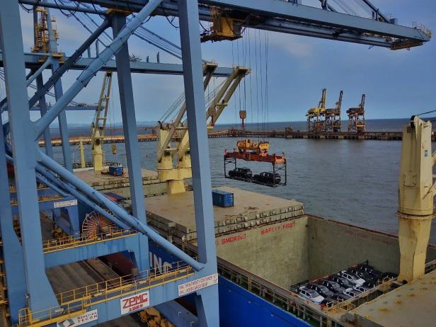 Kran hebt ein Gestell mit zwei Autos auf ein Containerschiff.