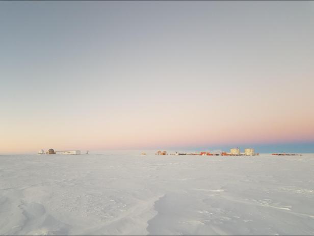 Die Amundsen-Scott-Südpolstation liegt in einer weiten, schneebedeckten Eislandschaft unter einem pastellfarbenen Dämmerungshimmel.