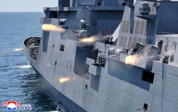 Kriegsschiff auf See feuert mehrere Geschütze und erzeugt Mündungsfeuer.
