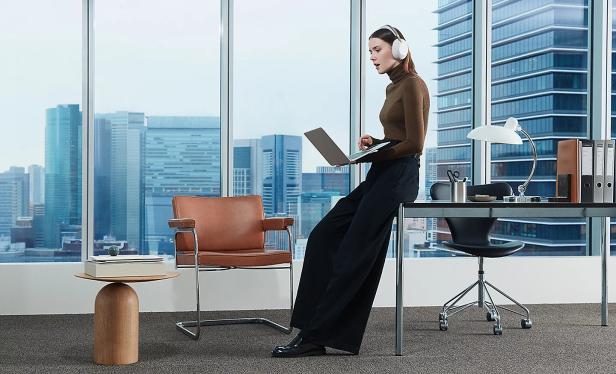 Frau mit weißen Over-Ear-Kopfhörern in modernem Büro mit Laptop.