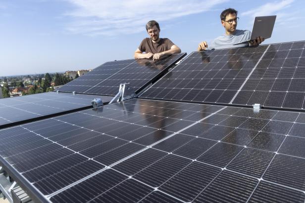 Zwei Männer stehen mit einem Laptop hinter halb zusammengefalteten Solarpaneelen