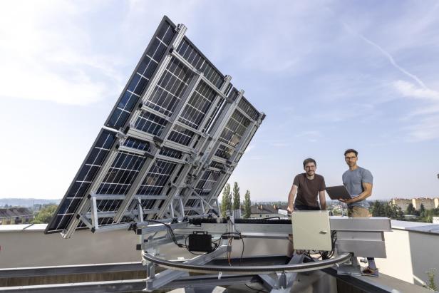 Zwei Forscher der TU Graz stehen neben der FLAPTrack-Anlage mit aufgeklappten, drehbaren Solarmodulen auf einem Dach.