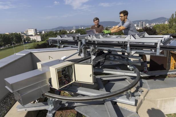 Zwei Forscher der TU Graz stehen neben der FLAPTrack-Anlage mit aufgeklappten, drehbaren Solarmodulen auf einem Dach.