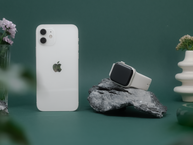 Ein weißes iPhone und eine Apple Watch auf einem Stein vor einem dunkelgrünen Hintergrund.
