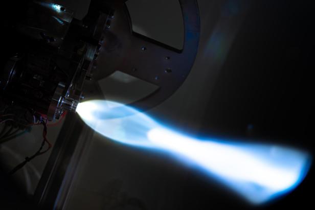 Ein kleines Raketentriebwerk erzeugt einen blauen Schubstrahl, wie er für den Satellitenantrieb von Beaconsat genutzt wird.
