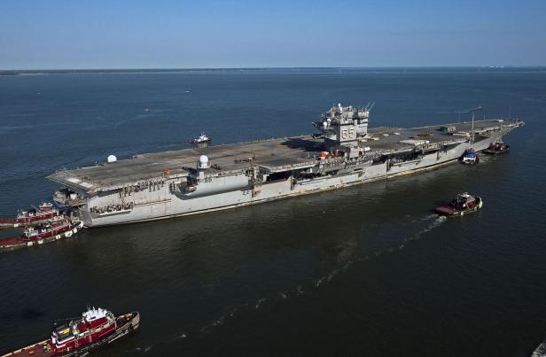 Der Flugzeugträger USS Enterprise wird von mehreren Schleppern auf dem Wasser manövriert.
