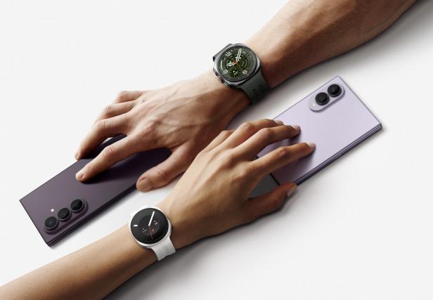 Zwei Hände berühren zwei faltbare Samsung-Handys neben zwei Smartwatches.
