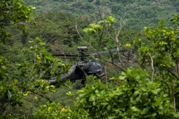Kampfhubschrauber fliegt tief über dicht bewaldetem Hang.