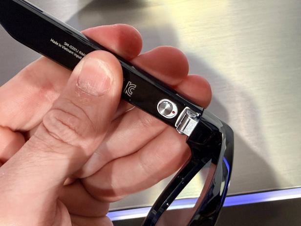 Eine Hand hält eine schwarze Smart-Brille mit breitem Bügel.