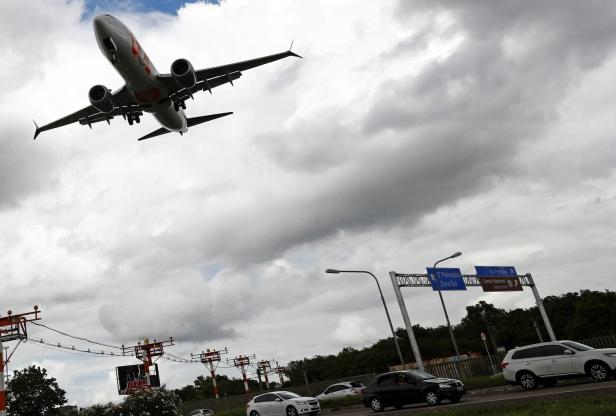 Passagierflugzeug im Anflug über einer Straße mit Autos und Wegweisern unter wolkigem Himmel.