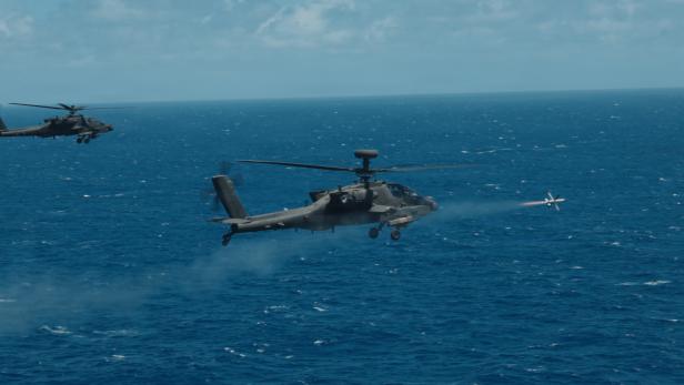 Ein AH-64 Apache der US Army feuert bei RIMPAC eine Rakete über dem Meer ab, begleitet von einem zweiten Kampfhubschrauber.