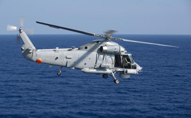 Ein grauer Militärhubschrauber fliegt knapp über dem Meer.
