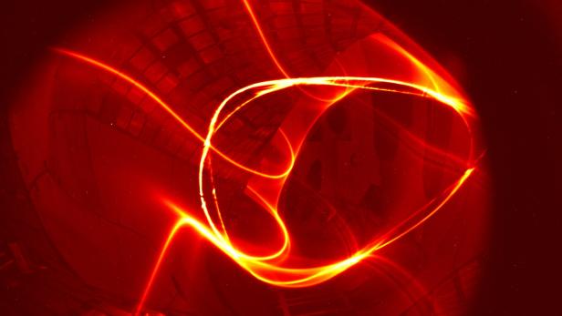Das Magnetfeld von Wendelstein 7-X (Juli 2015): Das Foto kombiniert die Leuchtspur eines Elektronenstrahls auf seinem vielfachen Umlauf längs einer Feldlinie durch das Plasmagefäß mit den Bildpunkten, die er auf einem fluoreszierenden Stab hinterlässt, der durch die Bildebene geschwenkt wird.