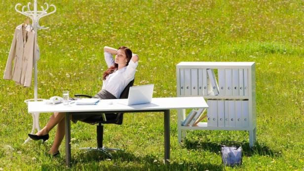 Young businesswoman in sunny meadow nature office relaxing behind table