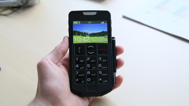 Eine Hand hält ein Mobiltelefon mit großen Tasten und einem Display, das eine Berglandschaft zeigt.