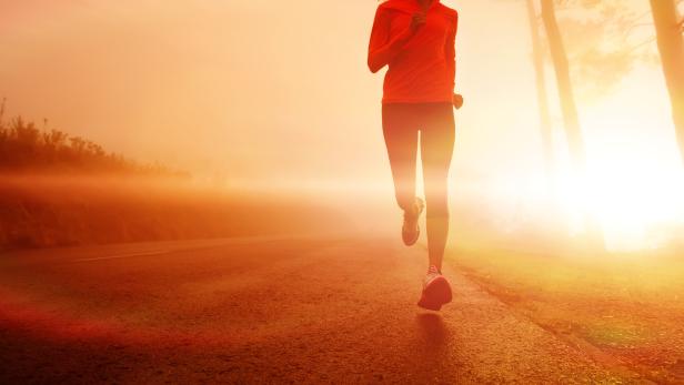 Eine Frau in Sportkleidung läuft auf einer Straße im goldenen Morgenlicht.
