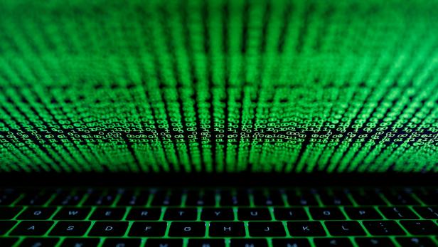Ein Laptop-Bildschirm zeigt grünen binären Code vor einer beleuchteten Tastatur.