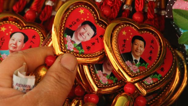 A woman picks a souvenir necklace with a portrait of Chinese President Xi Jinping from a selection that also includes necklaces featuring late Chinese Chairman Mao Zedong at a stall in Beijing