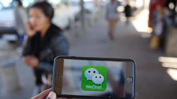 FILE PHOTO - A WeChat logo is displayed on a mobile phone as a woman walks past as she talks on her mobile phone at a taxi rank in this picture illustration