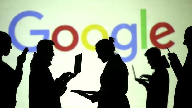 Silhouettes of laptop and mobile device users are seen next to a screen projection of Google logo in this picture illustration