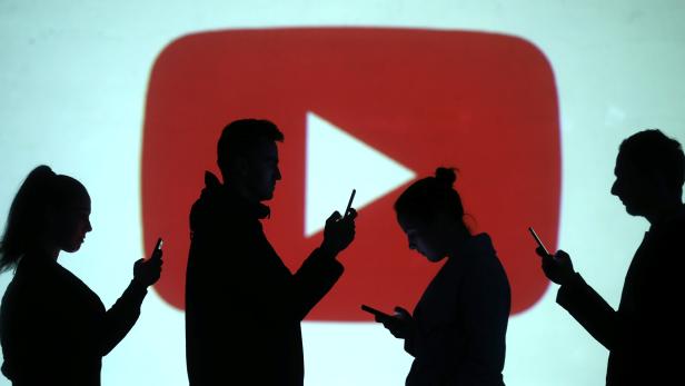 Silhouettes of mobile users are seen next to a screen projection of Youtube logo in this picture illustration