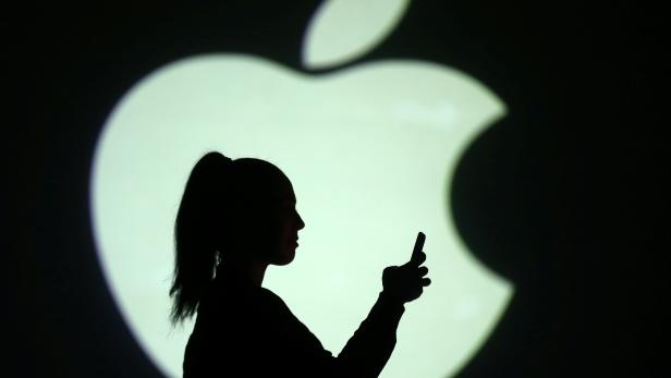Silhouette of mobile user is seen next to a screen projection of Apple logo in this picture illustration