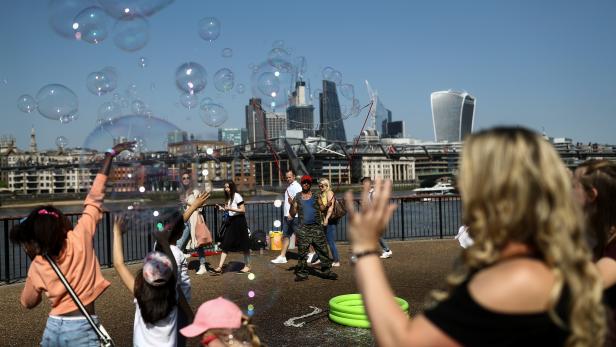 People try to pop bubbles from a street performer on the Southbank in view of London financial district in London