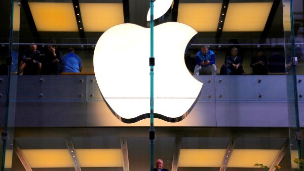 FILE PHOTO: A customer stands underneath an illuminated Apple logo as he looks out the window of the Apple store located in central Sydney
