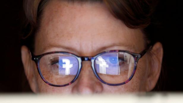 The Facebook logo is reflected on a woman's glasses in this photo illustration
