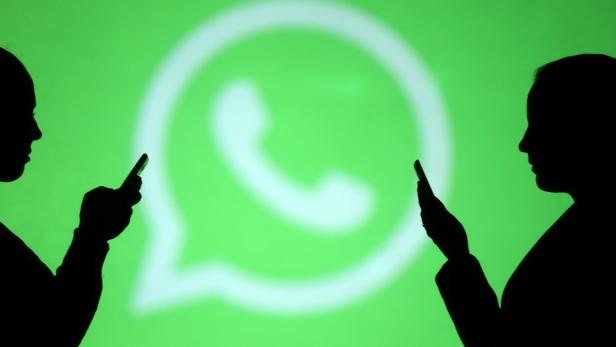 Silhouettes of mobile users are seen next to a screen projection of Whatsapp logo in this picture illustration