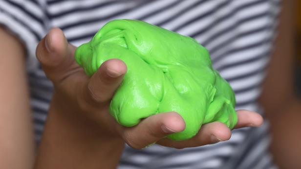 Ein Kind hält grünen Schleim in der Hand.