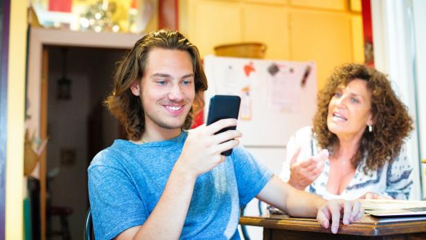 Male teenager oblivious to mother using mobile phone